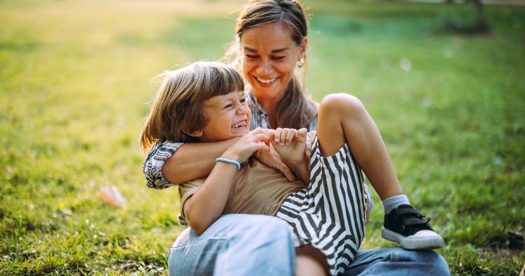 A young mom cheerfully holds her son while they play in the park.