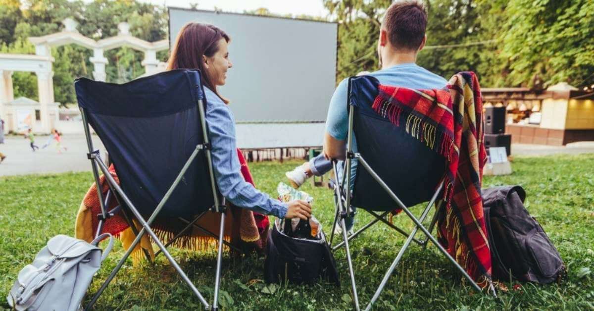 A young couple relax while watching a summer movie in the park.