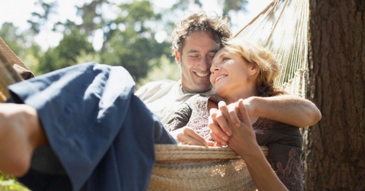 An older couple relax together in a hammock.