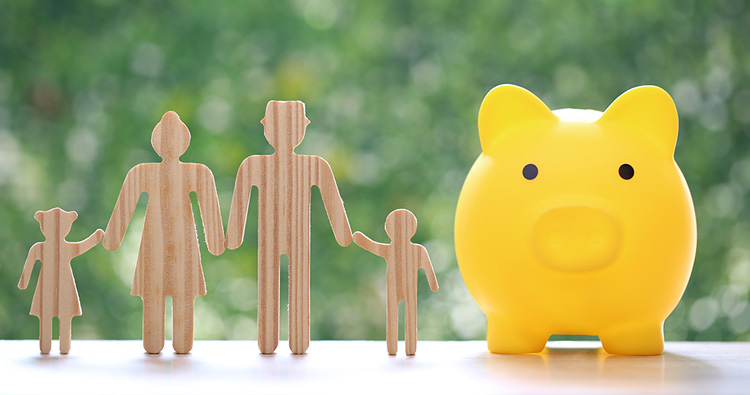 An image of a wood cutout of a family next to a yellow piggy bank