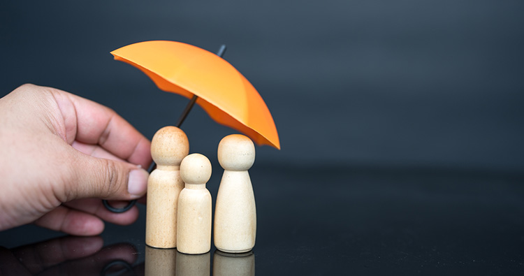 a close-up image of a hand holding a mini yellow umbrella over three wooden people figurines
