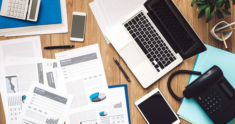 an overhead image of a table cluttered with papers, a laptop, files, a calculator, and telephone