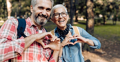 An older couple smile while shaping hearts with their hands