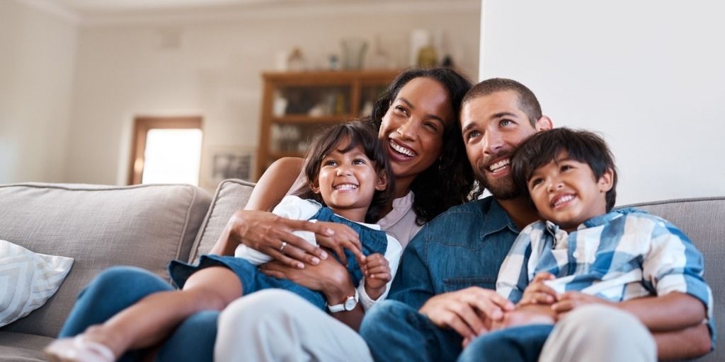 A young family embrace on the couch together with big smiles