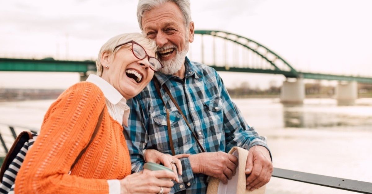 An older couple embrace while laughing near a bridge