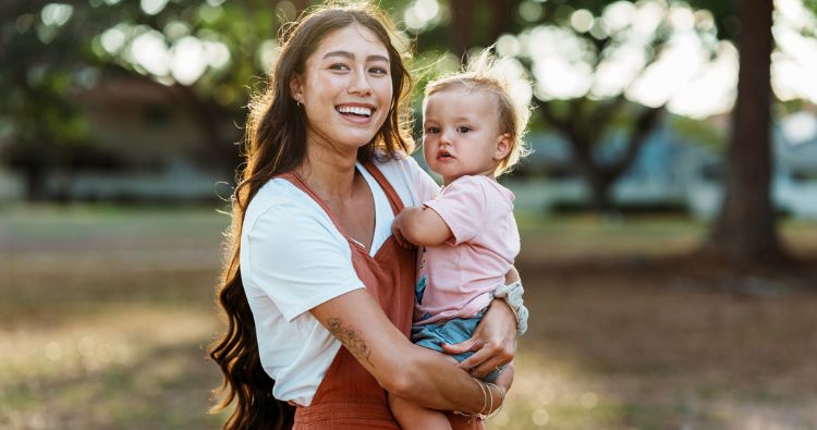 A woman smiles while holding a young toddler