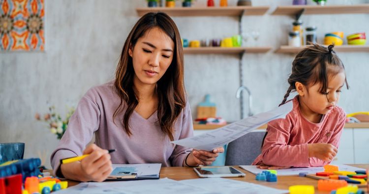 A mother looking at her finances with her young daughter sitting next to her