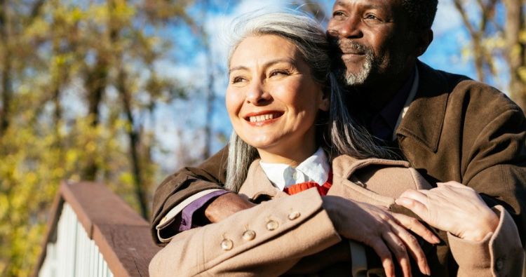 A retirement-aged couple embrace while looking at the sunset.