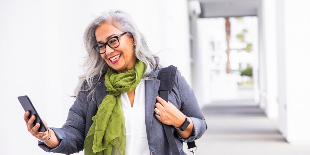 silver haired woman with green scarf, smiles on video call