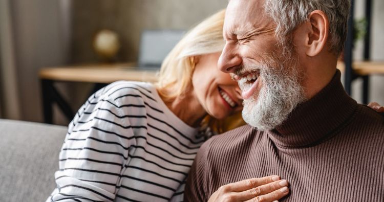 A retired couple laught together in a loving embrace.