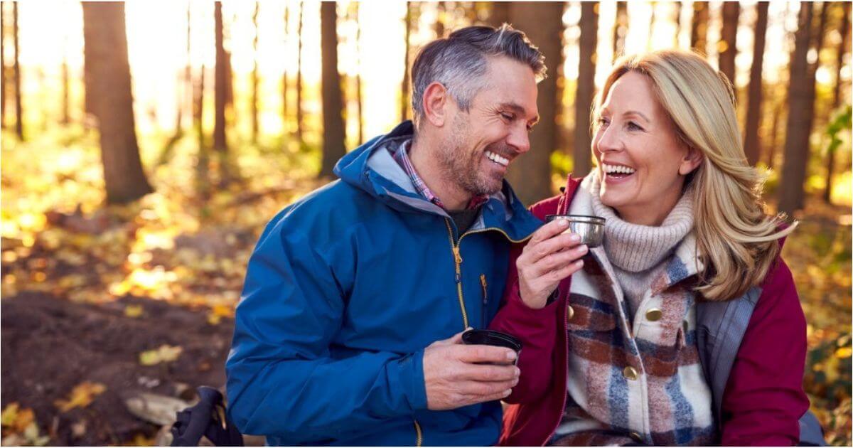 A retireed couple smile while enjoying coffee outside.