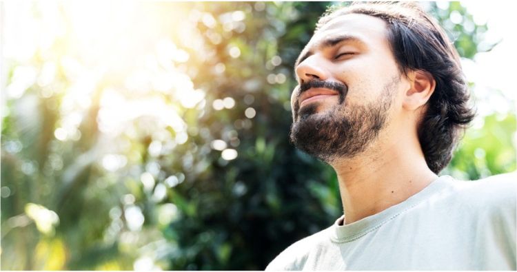 A man with closed eyes takes a relaxing breath in the woods