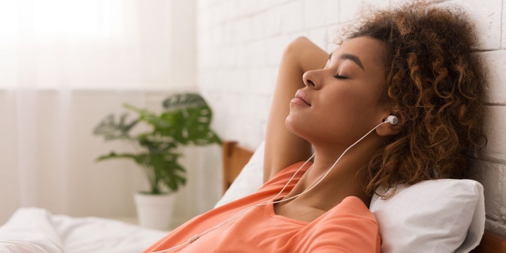young multi-racial female listens to music in bed during Covid 19