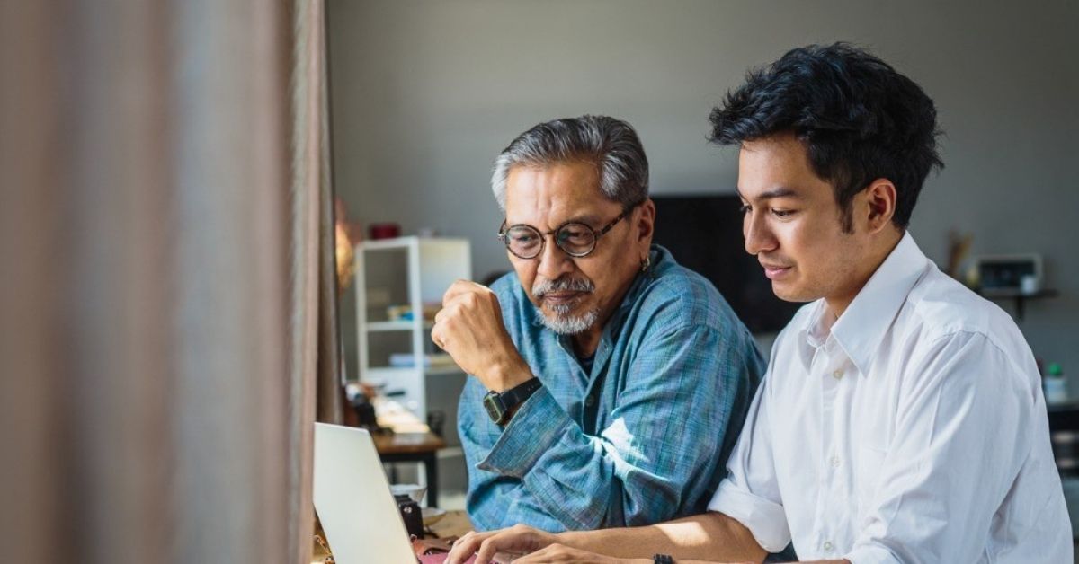A young man and his father work through finances on a computer.