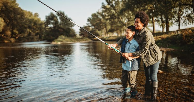 A mom teaches her son how to fish in a river
