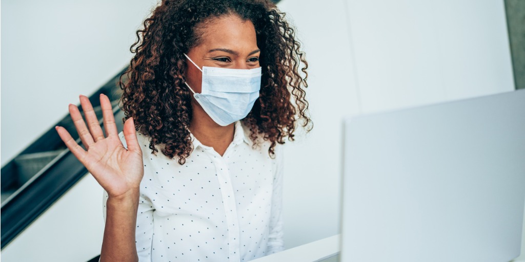 A young black woman wearing a mask waves during her webinar meeting