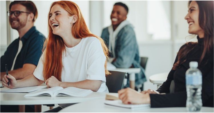 A group of college student smile while sitting in a lecture.