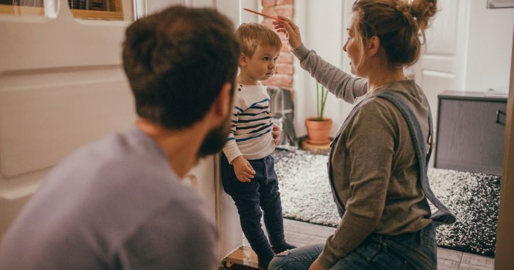 A young mom makes a mark a door post to measure her son's height