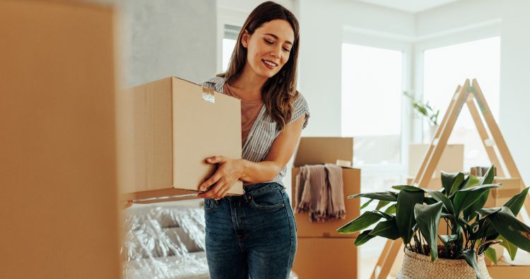 A woman holds a cardboard box while she moves into a new home.
