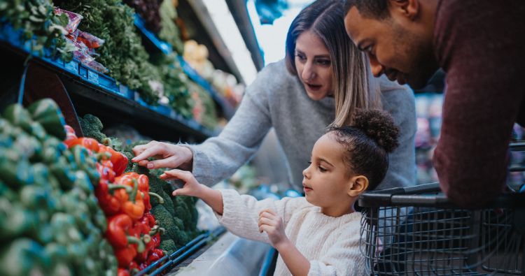Parents and their young daughter picking out fresh produce together in the grocery store