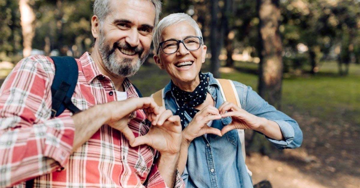 An older couple smile while shaping hearts with their hands.