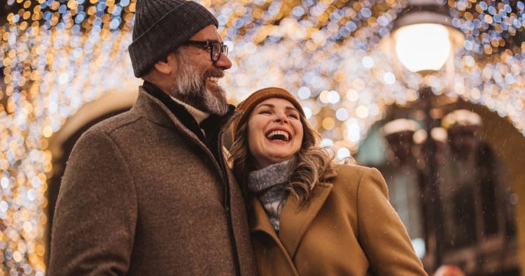 A couple walk down a street surrounded by holiday lights.
