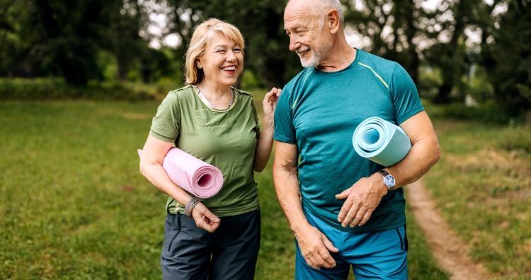An retired couple walk together holding yoga mats.