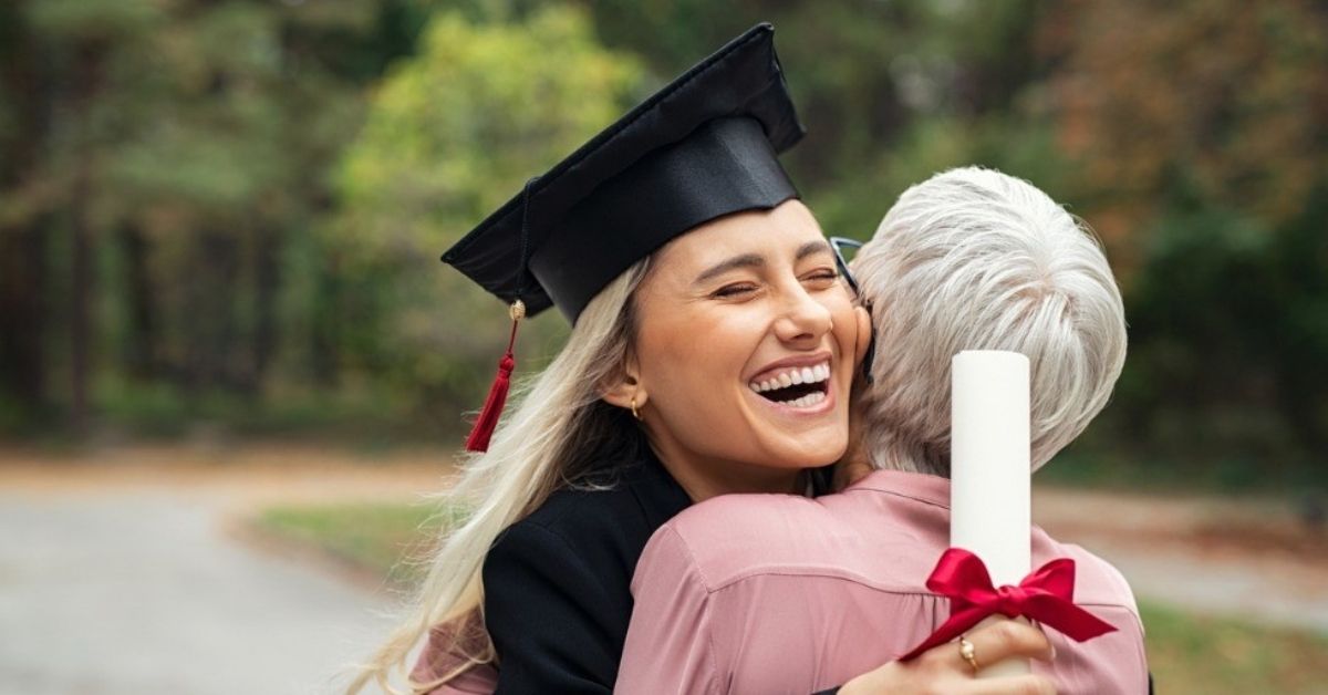 A young college graduate hugs her mom while holding a diploma