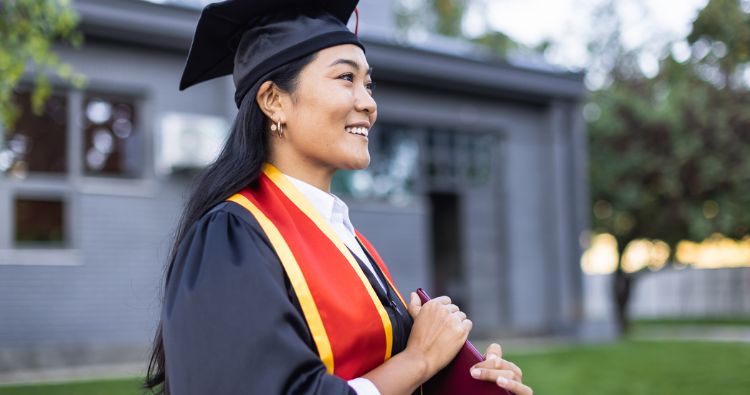 A young woman smiles brightly while holding her diploma.