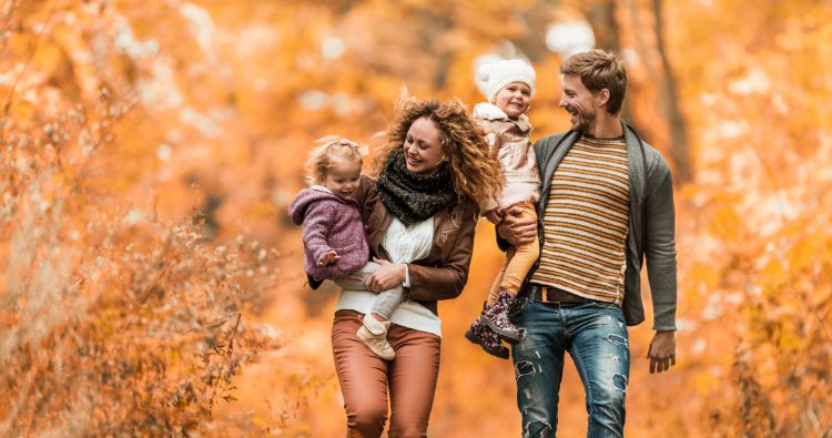 A family talk a walk surrounding by bright fall trees.
