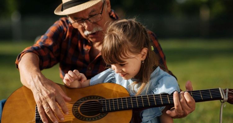 A grandfather teaches his daughter how to play guitar.