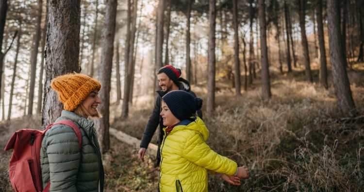 A family bundled up in winter gear take a hike in the woods.