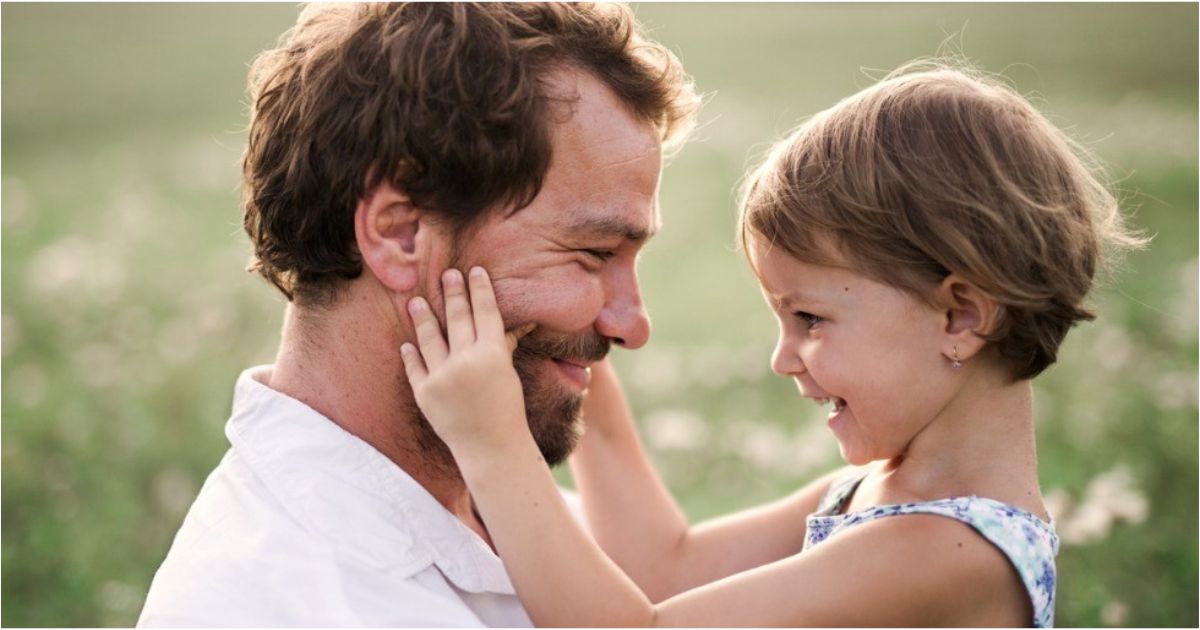 A father gives his toddler daughter a big smile while she touches his face.