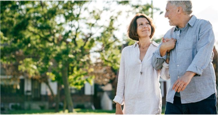 An older couple link arms while glancing at each other on a walk