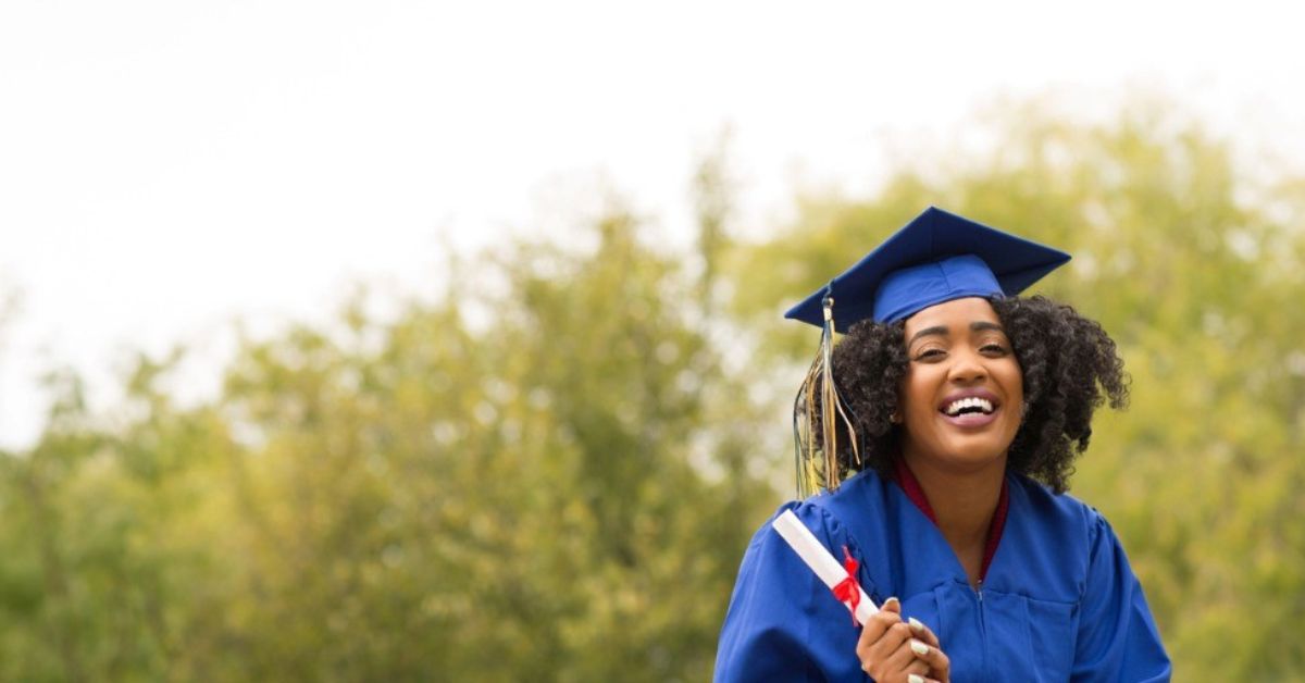 A young woman smiles brightly while holding her diploma.
