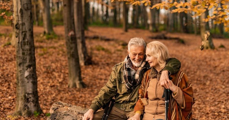 An older couple sit together in the woods surrounded by fall colors?