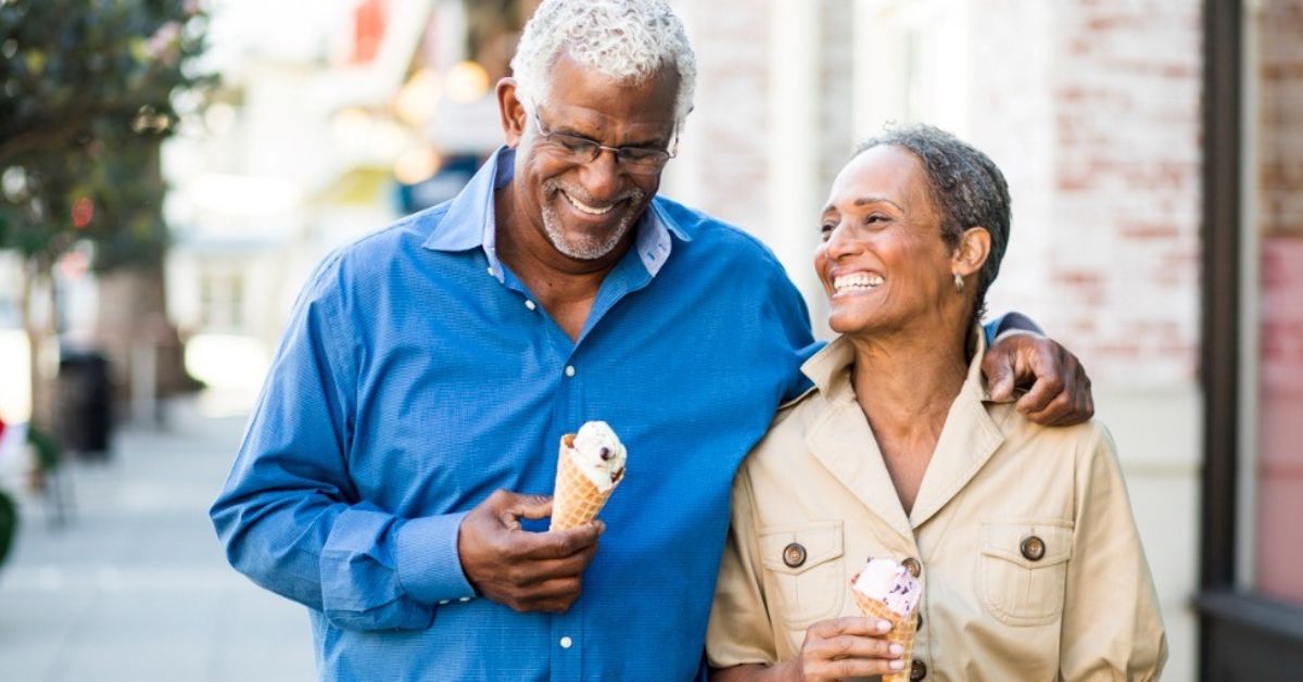 A retired couple smiles while walking together and eating ice cream.