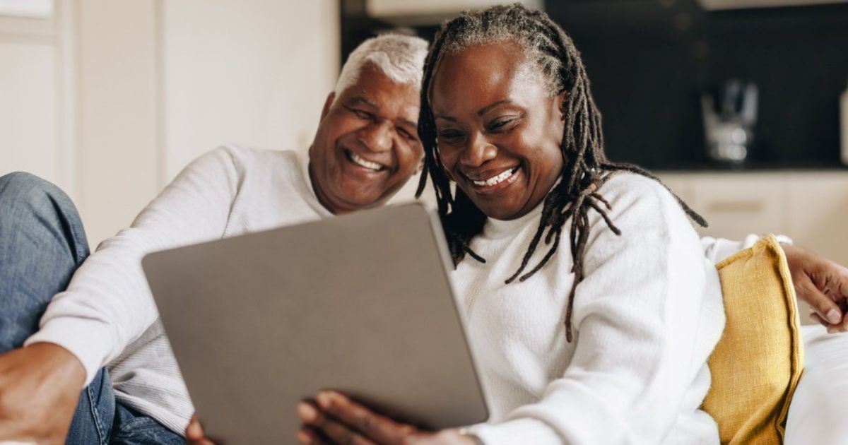 A retired couple smiles while reviewing their financial information.