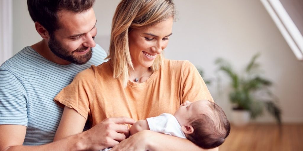 millennial couple cuddle newborn baby