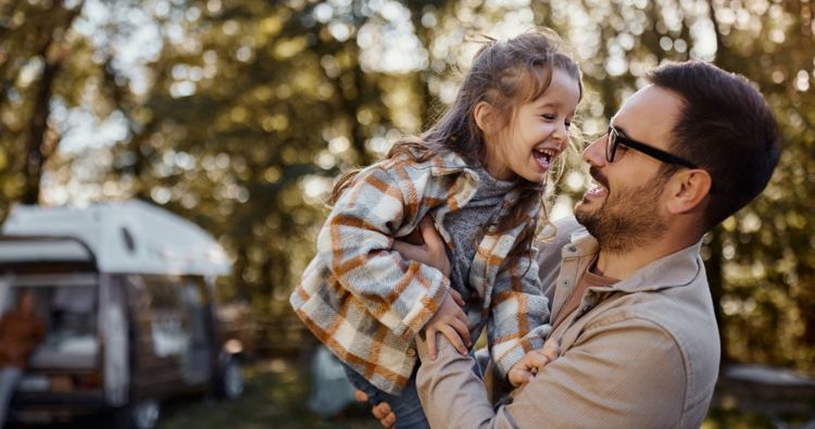 A father lifts his young daughter up while laughing.