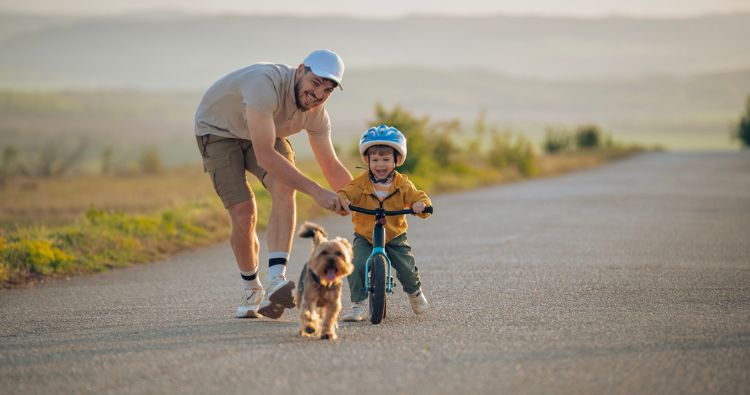 A father teaches his young son how to bike on an open road