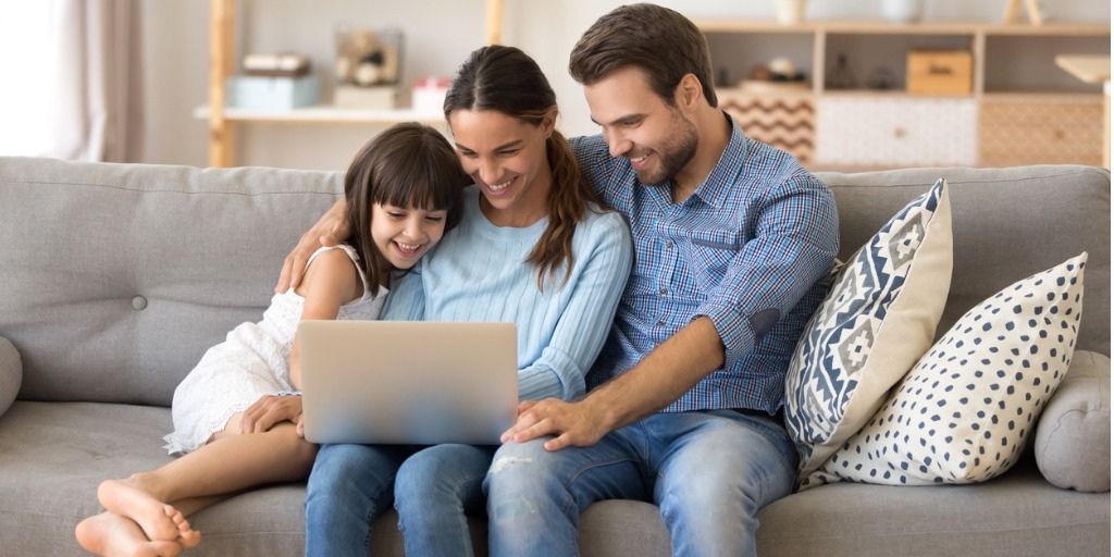 young family of three sitting on couch with laptop