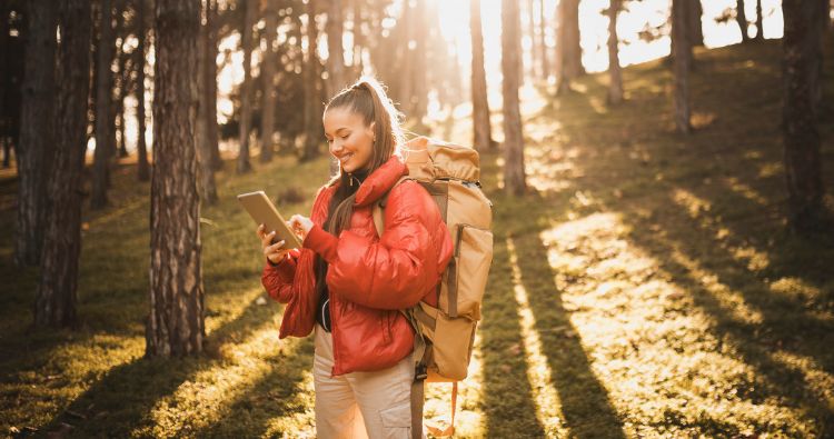 A woman looks at her tablet while walking in the woods.