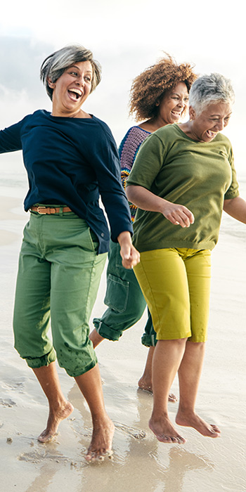 Three ladies smiling and jumping on a sandy beach