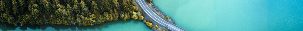 An aerial view of a road running through a forest and lake area.